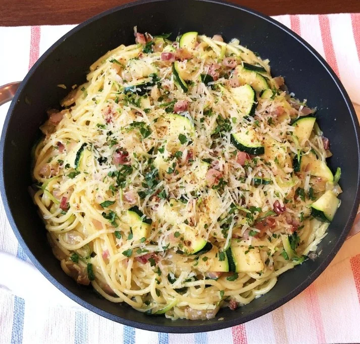 Pasta carbonara met courgette op een bord, versierd met kaas en kruiden.